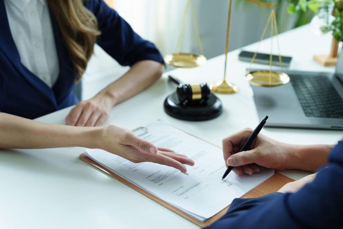 A professional guiding a client through signing documents at a table with scales of justice in the background