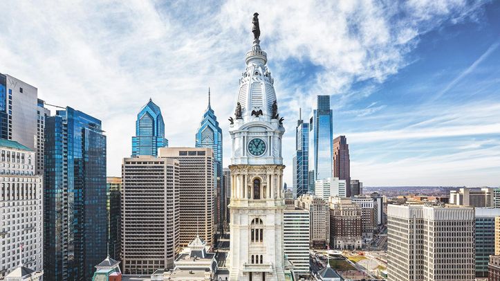 A historic city hall tower and skyline under a bright blue sky
